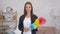 Close up portrait of cheerful young housewife holding colorful dust brush and smiling to camera at home