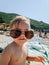 Close-up portrait of a child on the beach, wearing large sunglasses.