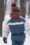 Close-up portrait of child in winter clothes. Boy stands his back in snowy forest