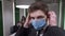 Close-up portrait of confident handsome man looking at camera putting on coronavirus face mask in office, colleagues at