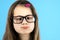 Close up portrait of a cross eyed child school girl wearing looking glasses isolated on blue background