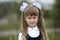 Close-up portrait of cute adorable smiling little first grader girl in school uniform and white bows in long blond hair on blurred