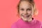 Close-up portrait of a cute blonde Caucasian teenage girl wearing a pink sweater, genuinely laughing and smiling at the