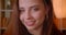 Close-up portrait of cute female student smiles into camera being modest and shy on bookshelves background.