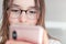 Close-up portrait of cute happy tween girl in glasses looking at smartphone in her hands.