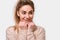 Close up portrait of cute kind young woman smiling and keeps hands on chin, looking aside, dressed beige sweater