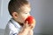 Close up portrait of cute little baby boy with atopic dermatitis on his cheek holding and eating red apple.