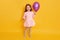 Close up portrait of cute little girl holding puple balloon and looks exited posing isolated over yellow background, charming