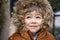 Close up portrait of cute little toddler boy in furry hood looking at snowfall