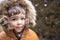 Close up portrait of cute little toddler boy with rosy cheeks in furry hood at snowfall outdoors