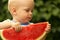 Close up portrait of cute toddler trying watermelon first time.