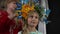 Close-up portrait of cute Ukrainian little girl in beautiful head wreath with blurred woman adjusting accessory in slow