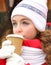 Close-up portrait of a cute young girl drinking hot tea in a red winter coat, a knitted white hat and gloves. Christmas. New year