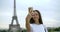 Close-up portrait of a dark-haired woman standing and posing against the Eiffel tower in Paris. She holds in her hands