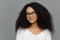 Close up portrait of delighted beautiful Afro woman with bushy curly hair, looks through transparent glasses, wears white sweater