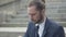 Close-up portrait of desperate man in formal suit drinking alcohol from flask outdoors sitting on urban city stairs