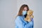 A close-up portrait of a doctor wearing an operating theatre outfit and brazing a teddy bear - isolated on a blue background.