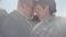 Close up portrait of an embracing adult married couple standing in the cool windy sunny weather on the background of