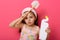 Close up portrait of exhausted serious kid standing isolated over pink background in studio, holding toilet brush and detergent,