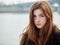 Close up portrait of fabulous redhead woman with long hair in yellow sweater black leather jacket on blurred river pier background