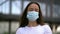 A close-up portrait of the face of a middle-aged woman with dark loose hair, wearing a protective medical mask. She is