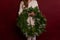 Close up portrait faceless young woman in knitted white sweater holds green Christmas wreath in hand