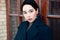 Close up portrait of a fashionable brunette woman with short hair and wearing a blue coat on the background of a door frame.