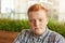 Close up portrait of fashionable redhead hipster man with freckles wearing checked shirt while posing in the cafe having serious e