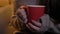 Close-up portrait of female hands holding red cup with hot drink on cosy home background.