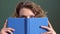 Close up portrait of a female student. Student girl hides behind the book. Woman reading a notebook and covering her