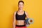 Close up portrait of fitness woman ready for workout, slim girl standing against yellow studio wall and holding yoga mat. Sporty