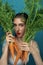 Close-up portrait of freckled female fashion model hiding behind carrot leaves