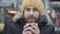 Close-up portrait of frozen young Caucasian man drinking hot coffee on the street. Cheerful guy in yellow hat and winter