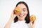 Close up portrait of funny asian girl, holds cupcakes near face, makes happy faces, white studio background