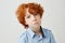 Close up portrait of funny little boy with red curly hair and freckles looking in camera with unhappy expression, after