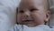 Close Up Portrait Of A Funny Newborn Baby Lying In Bed And Smiling