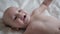 Close Up Portrait Of Funny Small Baby Smiling Playfully While Lying In White Bed