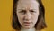 Close-up portrait of furious young woman looking at camera with rage and aggression on yellow background