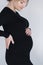 Close up portrait of gogreous pregnant woman in bkack dress hold her hand on belly and looks down