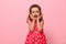 Close-up portrait of a gorgeous baby girl in a pink dress with polka dots poses at the camera, standing against a pink background