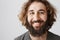 Close-up portrait of grinning emotive eastern male with long curly hair and beard smiling cheerfully, expressing