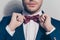 Close up portrait of half face - bearded stubble man ties a bowtie at the collar, correcting red bow on his white shirt over grey