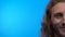 Close-up portrait half face. The modest long-haired man smiles tenderly. man on isolated blue background. 4K