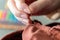 A close up portrait of a hand of someone holding a needle, sewing a hole in a pair of pants at the seam. The needle is about to be