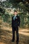 Close up portrait of handsome stylish groom outdoors in park with red bowtie