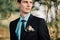 Close up portrait of handsome stylish groom outdoors in park with red bowtie