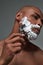 Close up portrait of handsome young african american man with foam applied on his face using steel razor for shaving