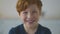 Close up portrait of happy adorable little redhead boy with freckles smiling and posing to camera