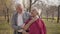 Close-up portrait of happy Caucasian retired couple standing in sunlight in the autumn forest and hugging. Mature