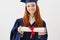 Close up portrait of happy foxy girl graduate in cap smiling holding diploma. Young redhead woman student future lawyer